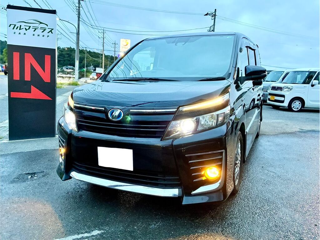 納車されたトヨタ ヴォクシー ハイブリッドのフロントビュー。ヘッドライト点灯